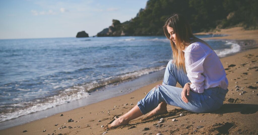 Woman sits on beach, gazing at waves having high functioning depression