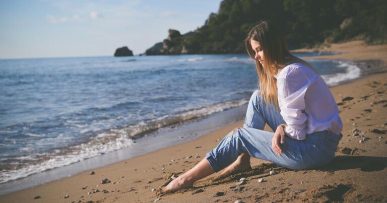 Woman sits on beach, gazing at waves having high functioning depression